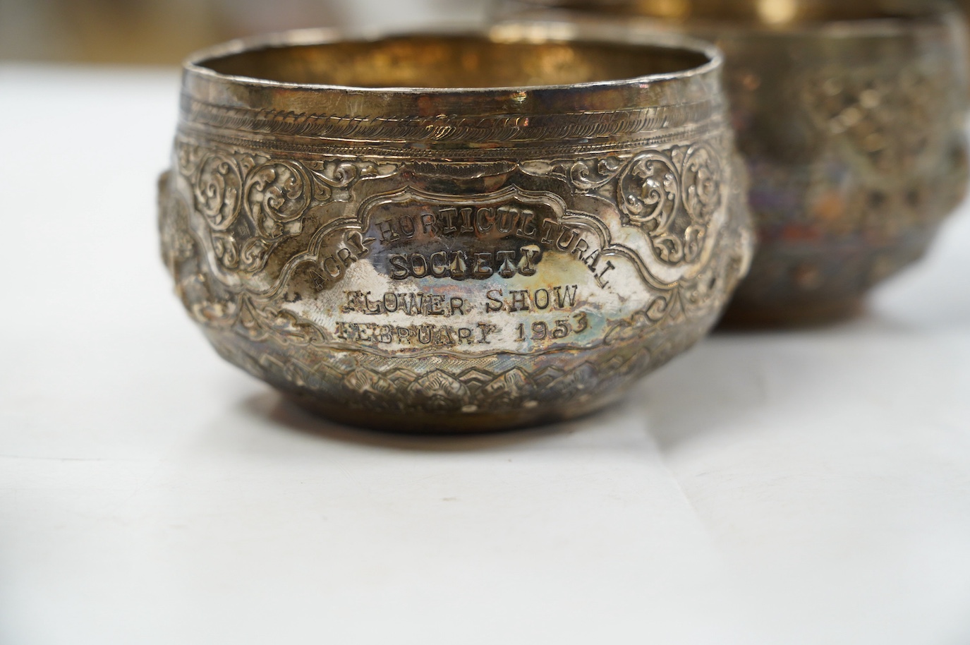 A pair of mid 20th century Indian embossed white metal small bowls, inscribed ' Agri-Horticultural Society Flower Show February 1953', diameter 10.4cm, together with a similar box and cover. Condition - poor to fair